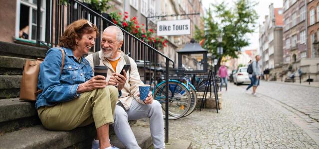Happy Senior Couple Tourists Sitting on Stairs and Having Take Away Coffee Outdoors in Town